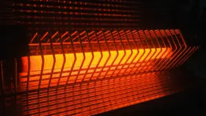 Kvēlojošs elektriskais sildītājs tumšā telpā, kas simbolizē apkures izmaksas un energoefektivitāti mājokļos.