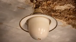 Veca griestu lampa ar nolietotu tekstūru un mitruma bojājumiem uz griestu virsmas.